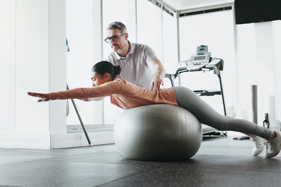 physiotherapy-woman-personal-trainer-gym-with-ball-challenge-stability-training-man-client-balance-fitness-center-core-strength-yoga-practice-help-exercise-growth
